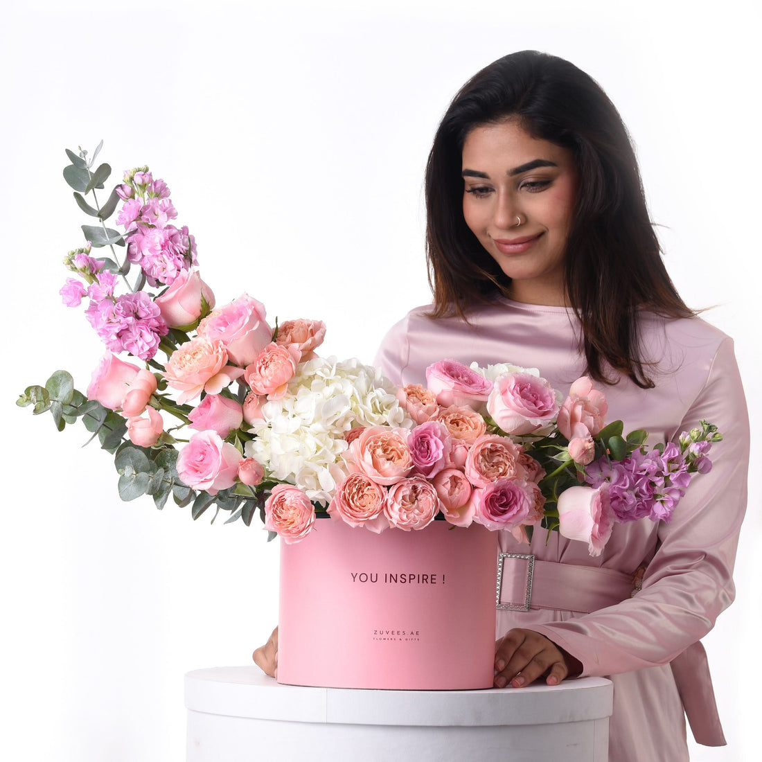 Pink floral arrangement in branded box, woman smiles, soft pastel tones.