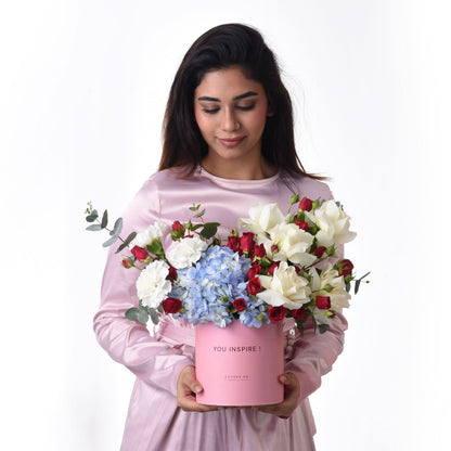 Pink box holds red, white roses and blue hydrangeas, with "YOU INSPIRE!" message.