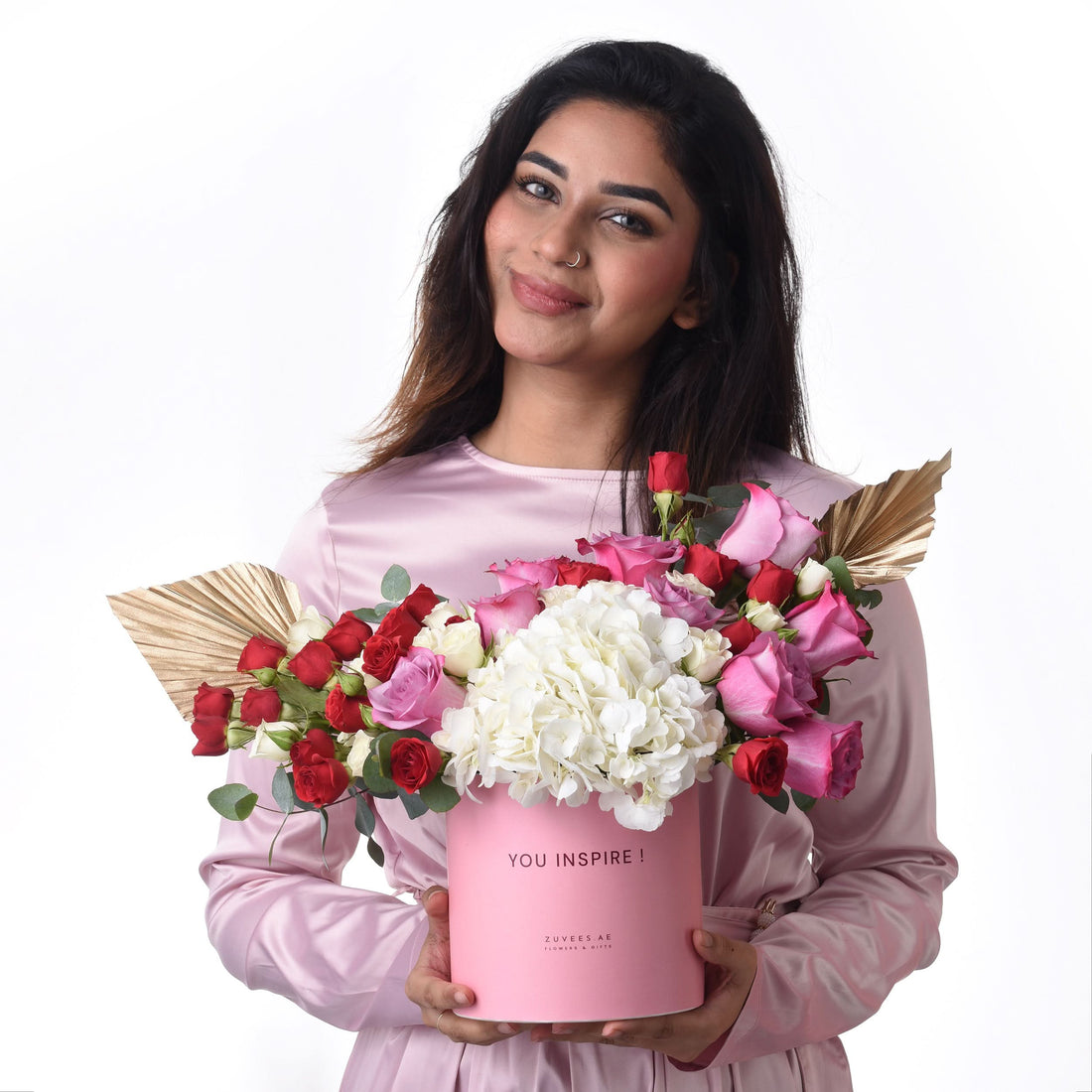Pink box holds vibrant red, pink, white roses and hydrangeas with gold leaf accents.
