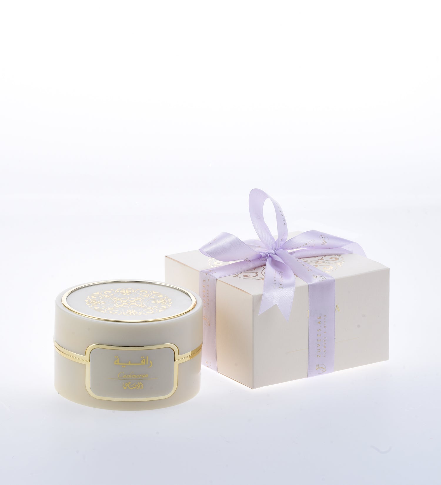 Cream jar with gold trim and Arabic label, beside lavender-bowed gift box.