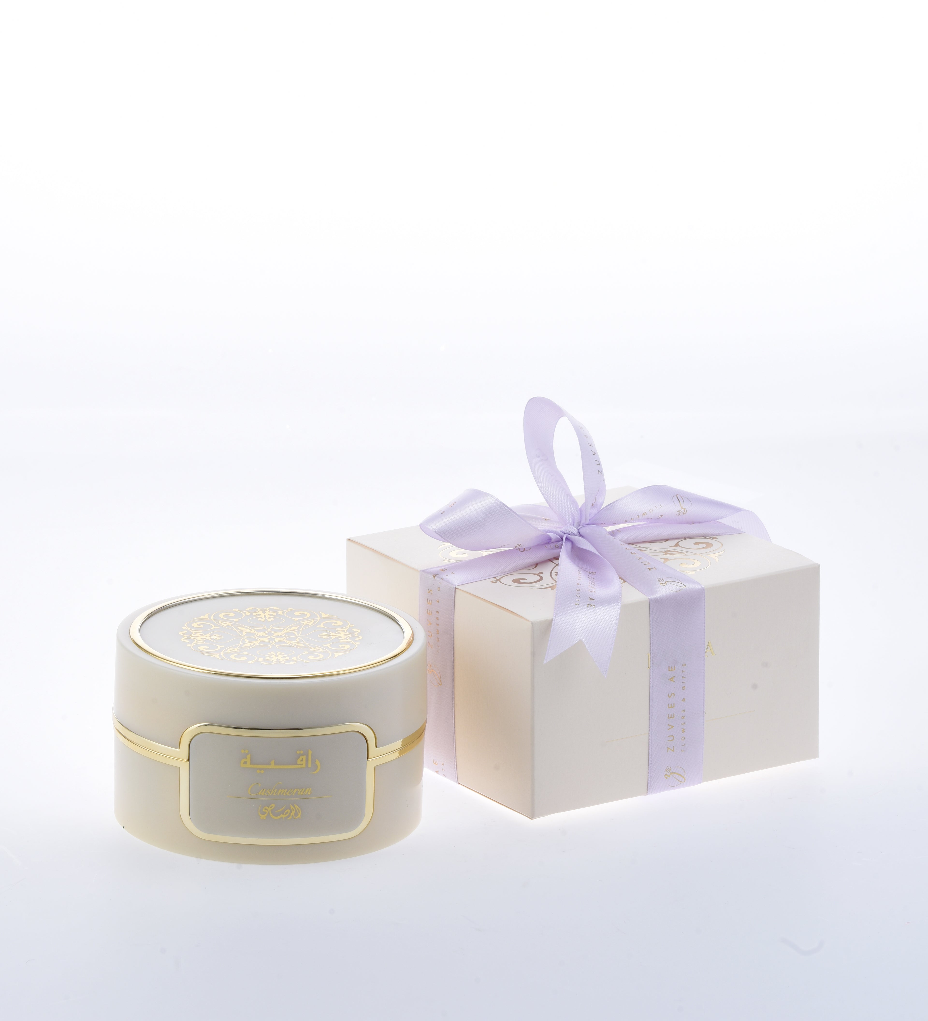 Cream jar with gold trim and Arabic label, beside lavender-bowed gift box.