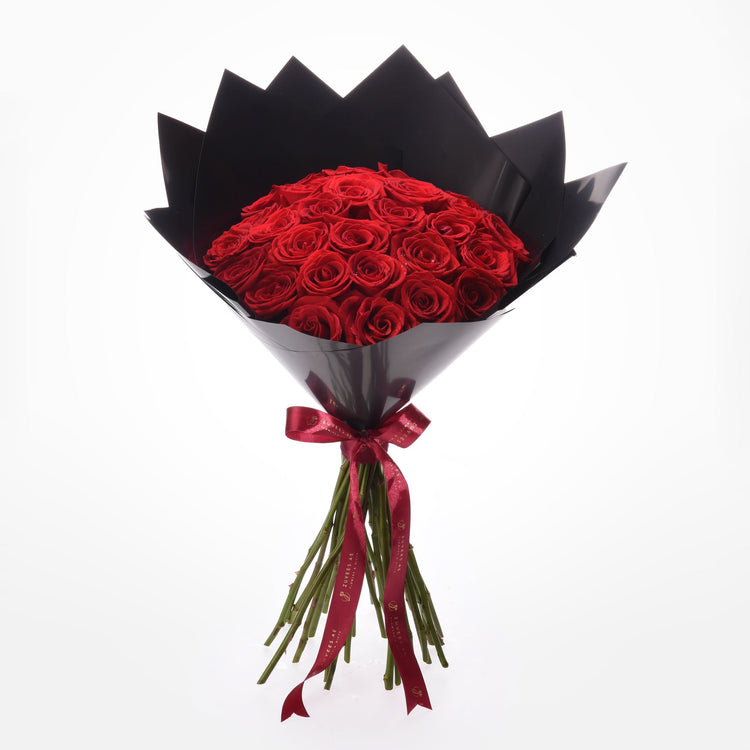 Vibrant red roses in glossy black paper, tied with elegant red ribbon.