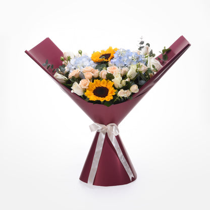 Vibrant sunflowers, roses, and hydrangeas in burgundy wrap with silver bow.
