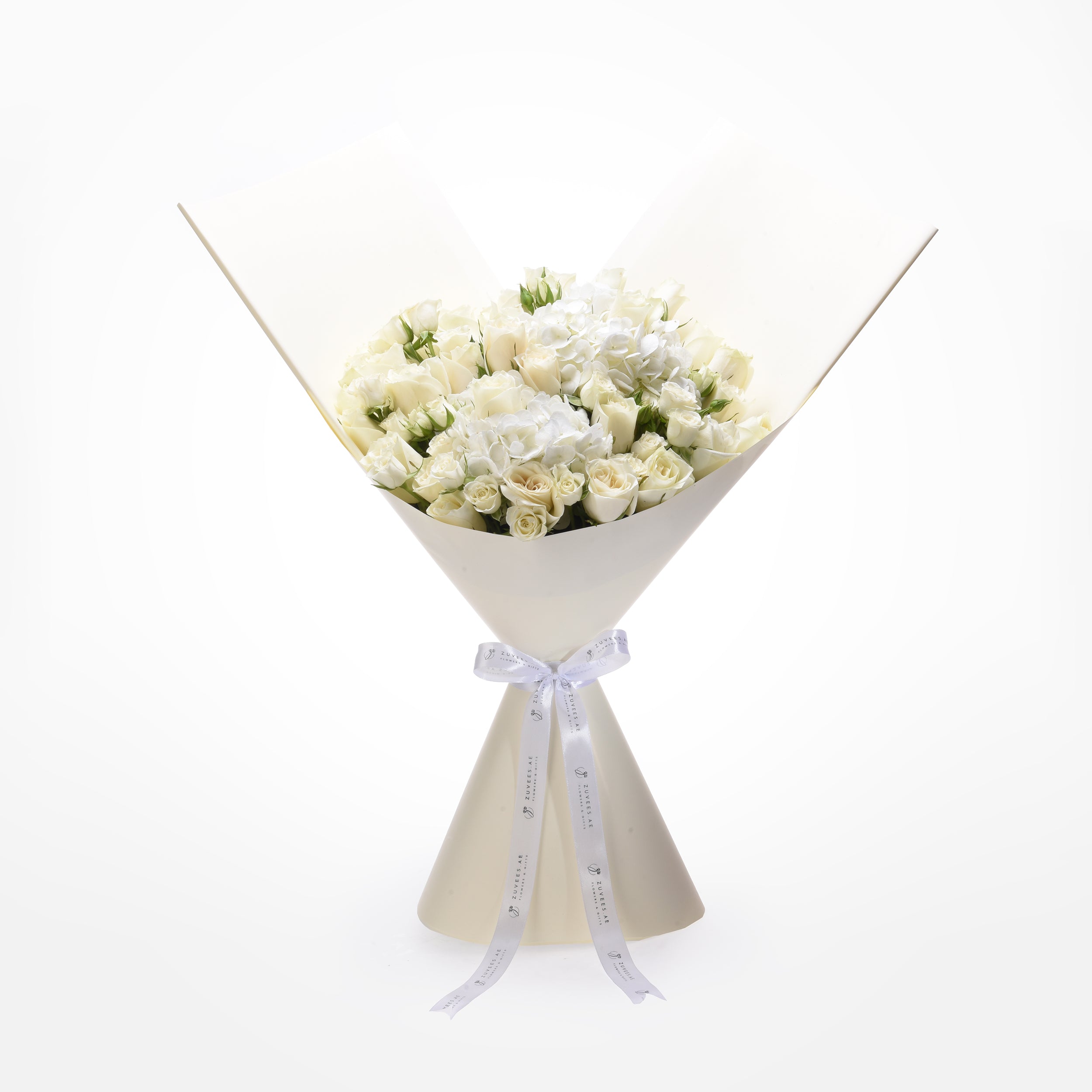 Elegant white rose bouquet with hydrangeas, wrapped in cream paper, tied with branded ribbon.