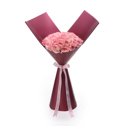 Soft pink roses in deep burgundy wrap, tied with branded ribbon.