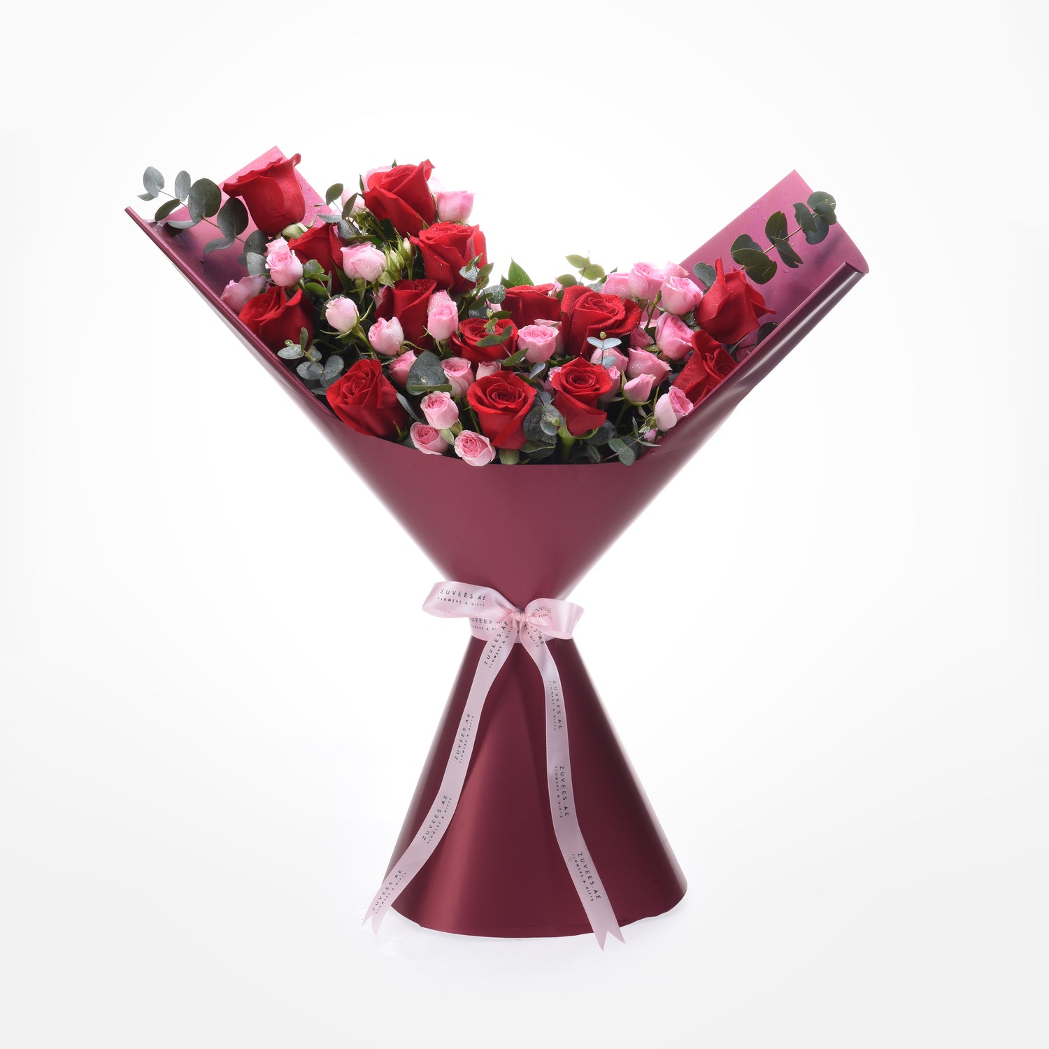 Vibrant red and pink roses wrapped in burgundy paper with elegant pink ribbon bow.