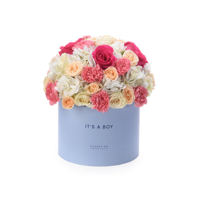 Pastel blue box overflowing with pink, peach, and white roses and carnations. "It&