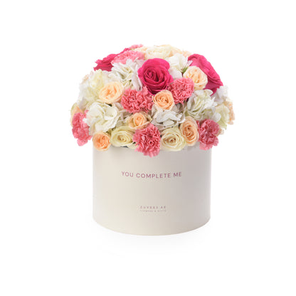 Cream box holds vibrant pink, peach, and white roses and carnations.