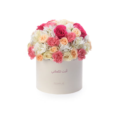 Cream box holds vibrant pink, peach, and white roses and carnations.