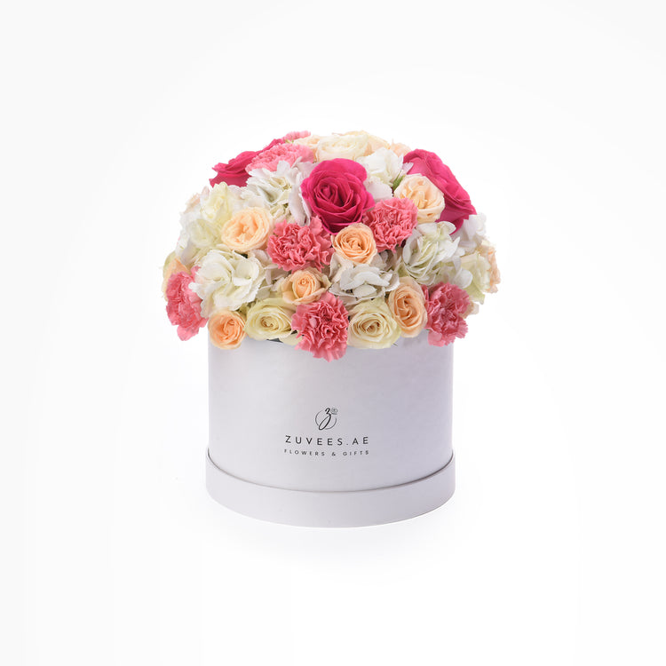 White box brimming with vibrant pink, peach, and white roses and carnations.