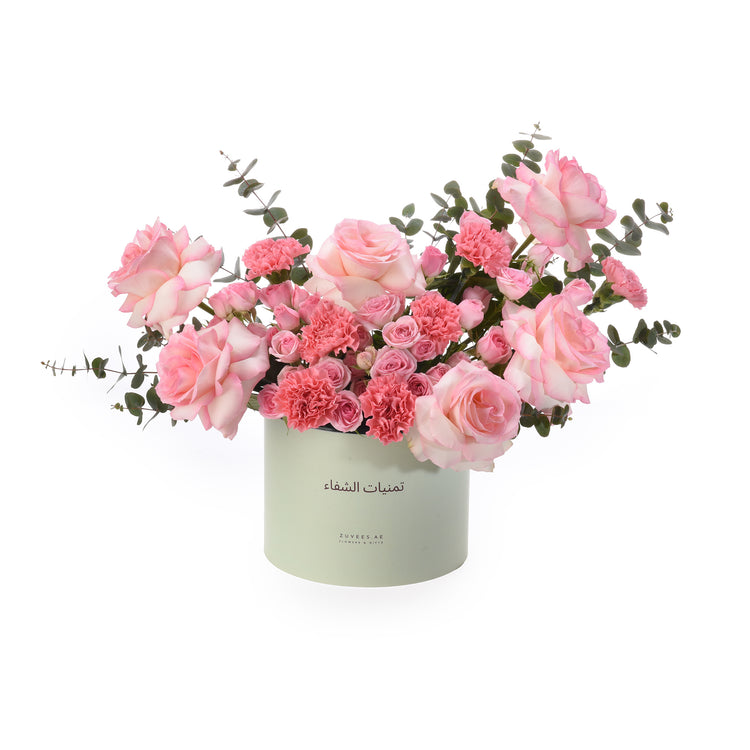 Soft pink roses and carnations in mint-green box with Arabic text.