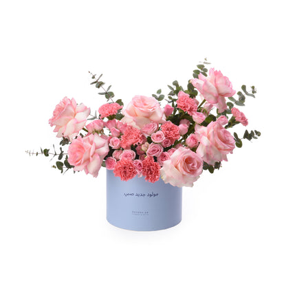 Soft pink roses and carnations in light blue cylindrical box with Arabic text.