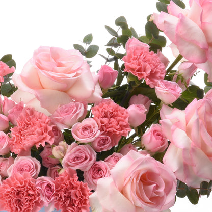 Soft pink roses and carnations with lush greenery, elegant floral arrangement.