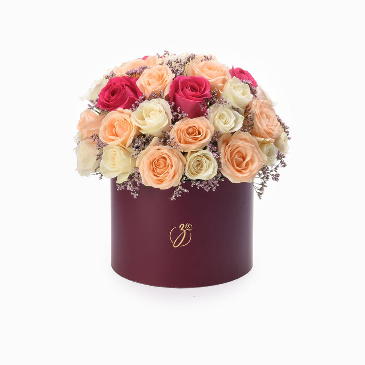 Elegant burgundy hat box filled with cascading peach, pink, and cream roses accented with lavender baby’s breath.