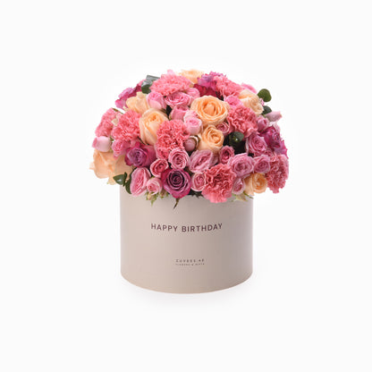 Pastel pink and peach roses and carnations in beige box with "Happy Birthday" text.