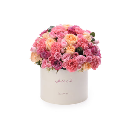 Cream box overflowing with vibrant pink, peach, and magenta roses and carnations.