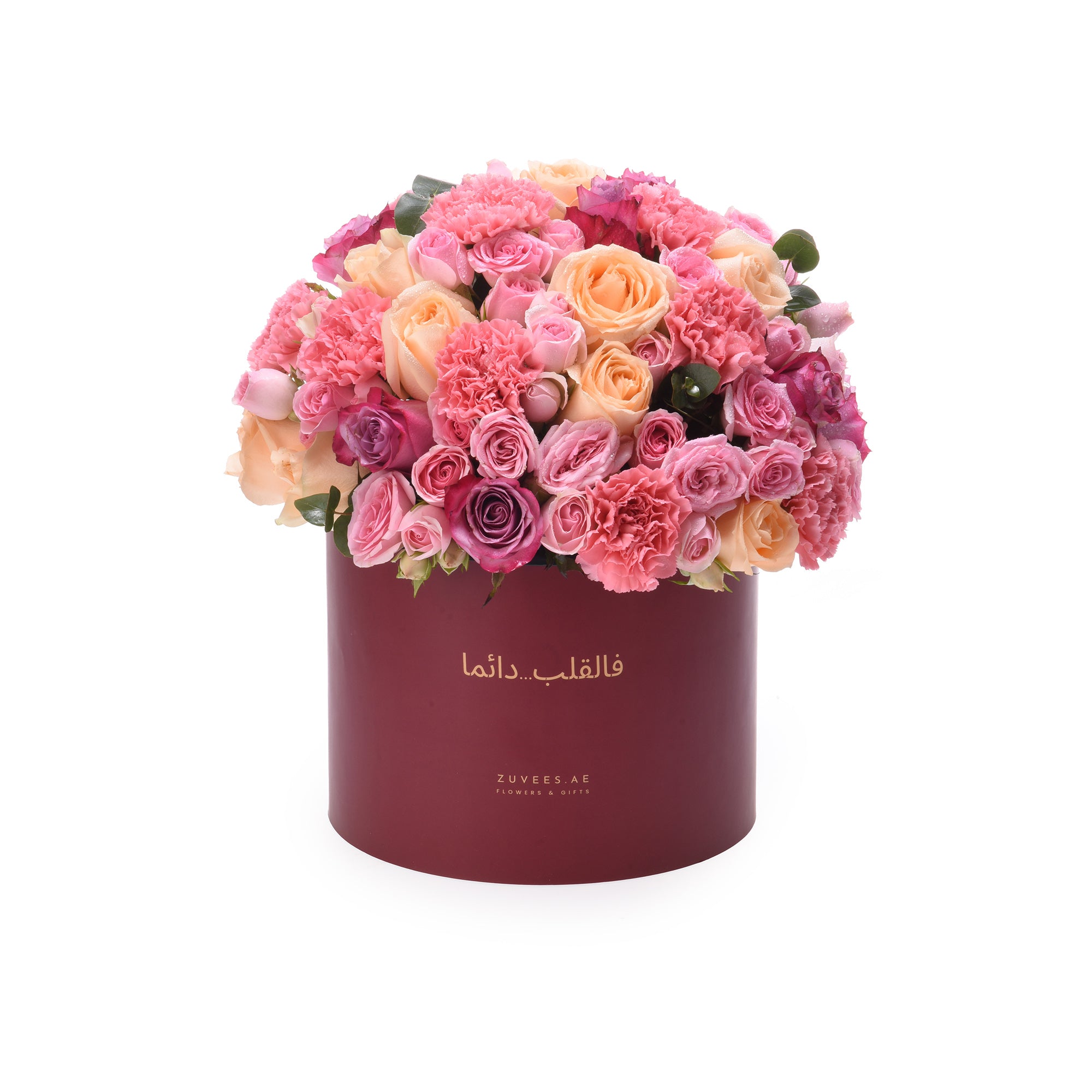 Vibrant pink, peach, and magenta roses and carnations overflowing from a deep burgundy hat box with gold Arabic script.