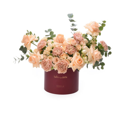 Luxury peach roses, carnations, eucalyptus in deep burgundy Zuvees box, elegant Arabic script.