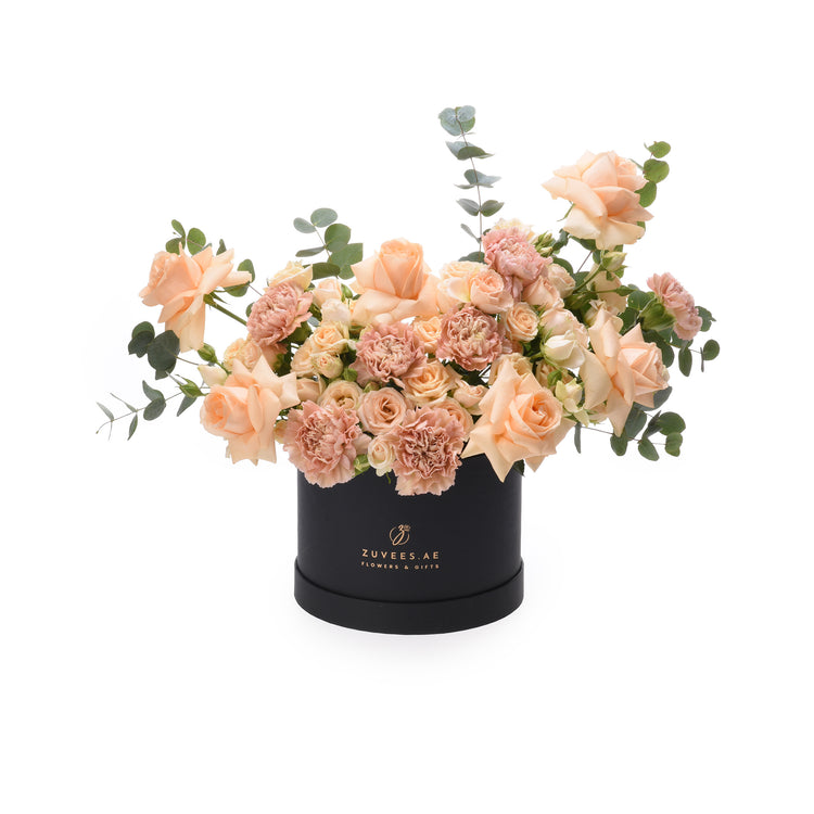 Elegant peach roses and carnations in sleek black box with gold branding.