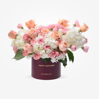 Soft pink roses and white hydrangeas in burgundy box with "Happy Birthday" gold text.