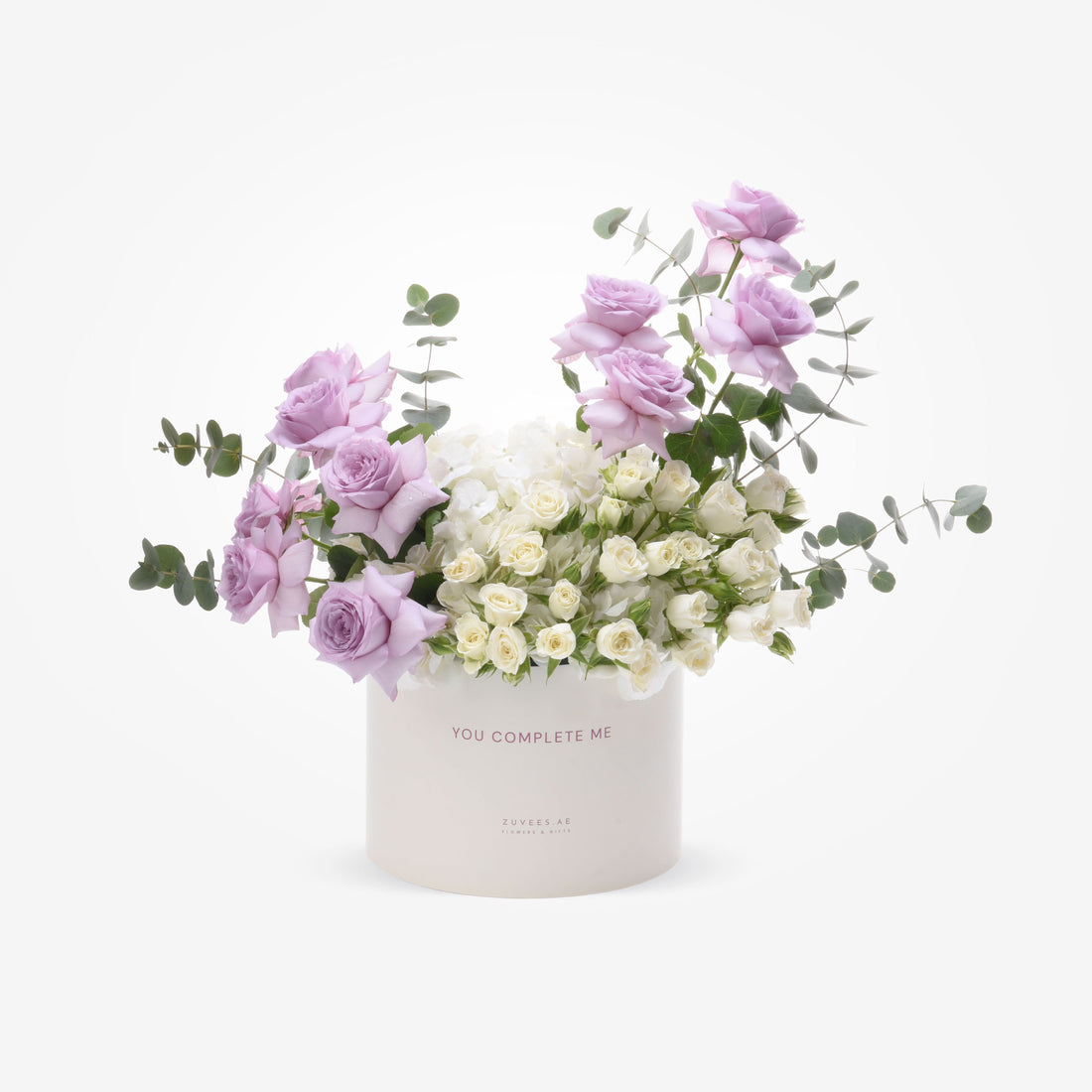 Soft lavender roses and white hydrangeas in minimalist white box with “YOU COMPLETE ME” inscription.
