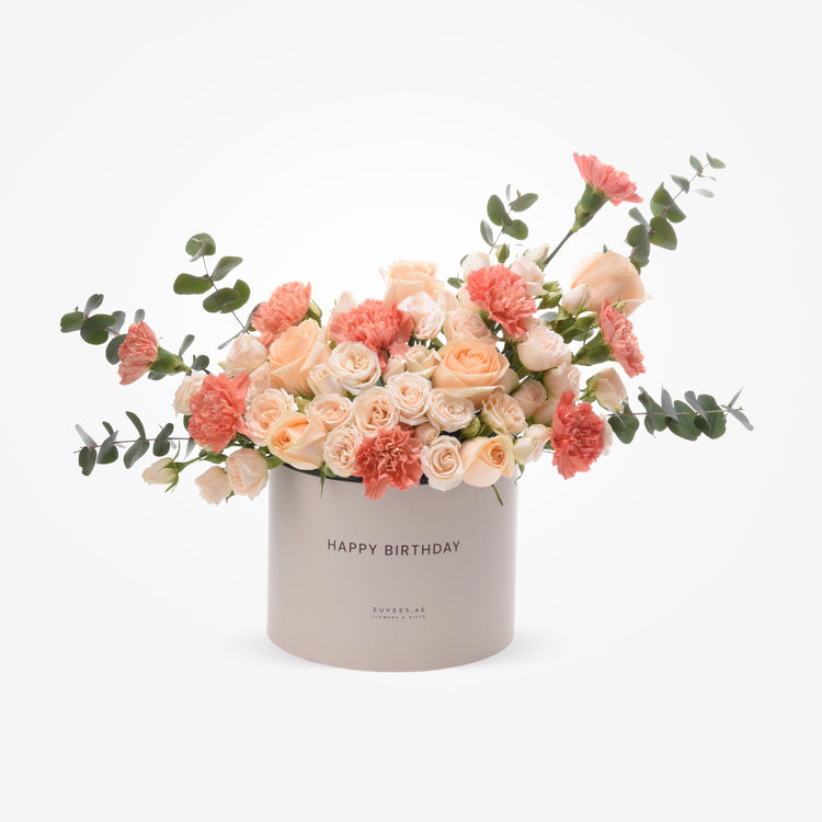 Pastel peach roses and carnations in sleek gray birthday box with eucalyptus.