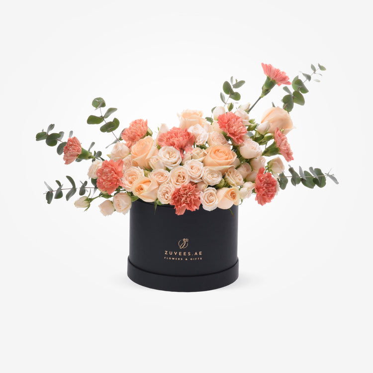 Elegant peach roses and carnations cascade from sleek black hat box.