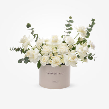 Elegant white roses and carnations in a blush "Happy Birthday" box with eucalyptus accents.